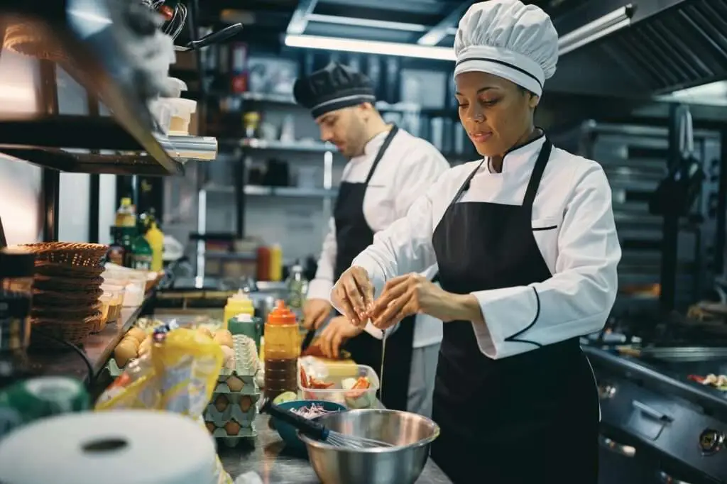 Black female chef cracking an egg while preparing food in a restaurant.