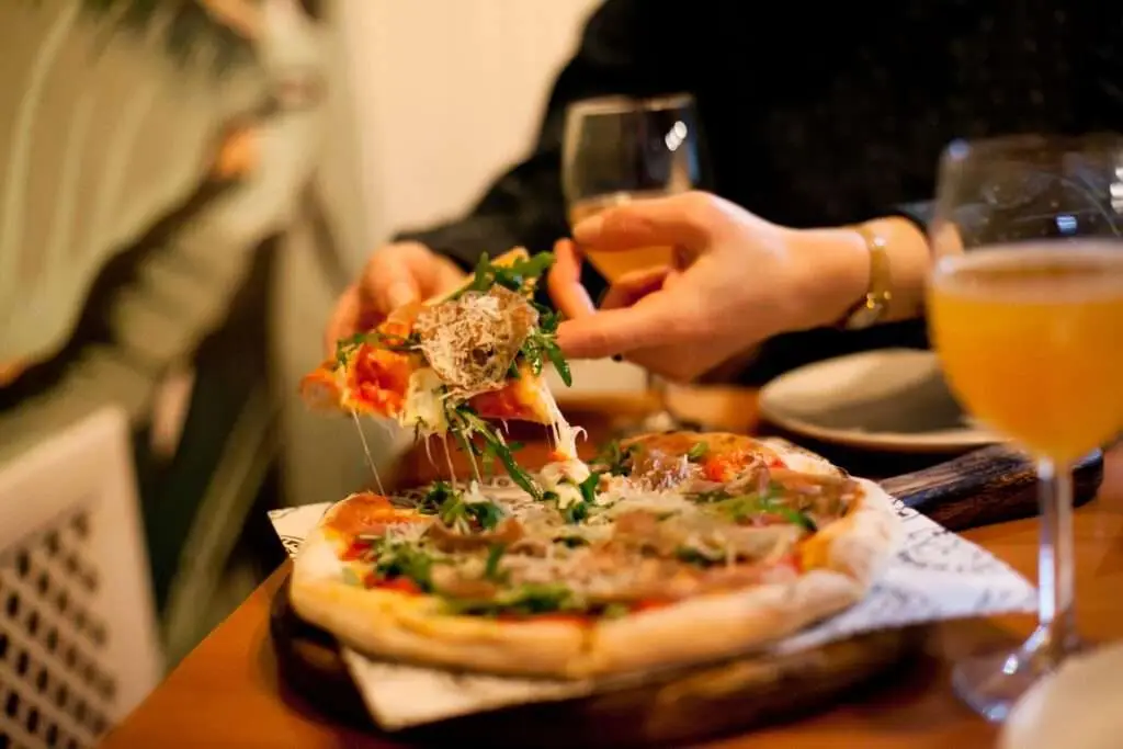 Woman eating pizza and drinking beer at the restaurant, food and drink