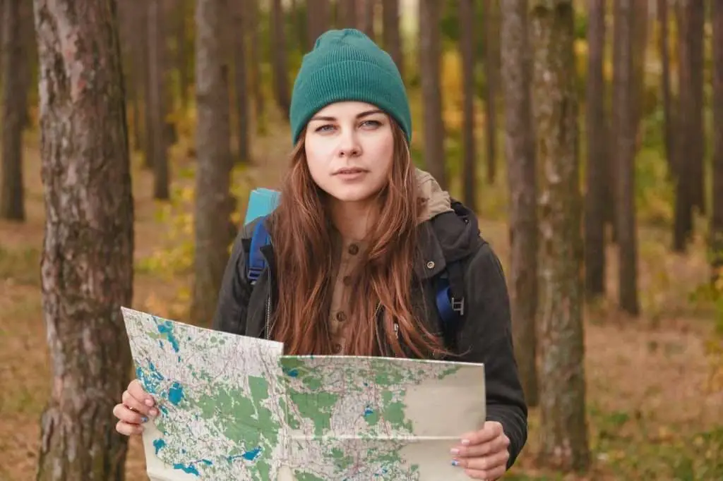 Woman with travel map and backpack in pine forest.